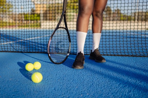 Low section of a tennis player standing on a vibrant blue court, holding a racket while tennis balls scatter across the ground, capturing the essence of athletic competition and training